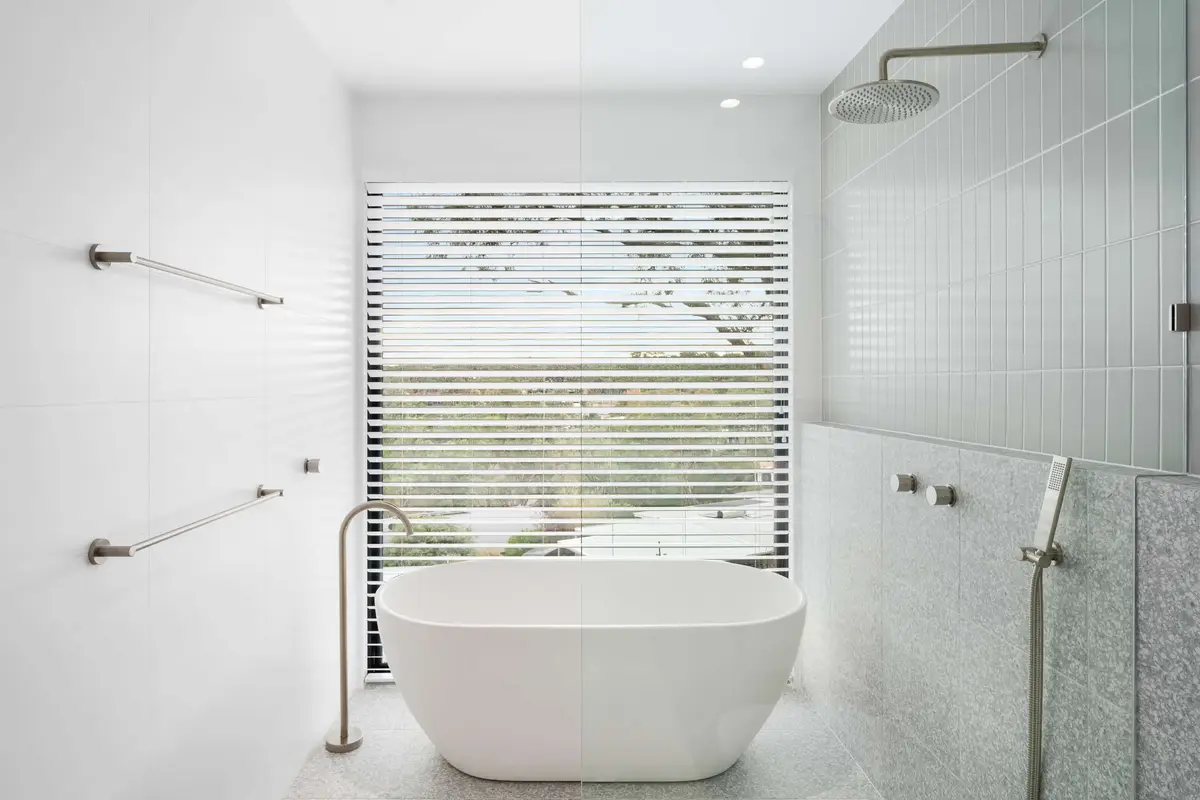 Freestanding bath framed by timber blinds overlooking the tree canopy